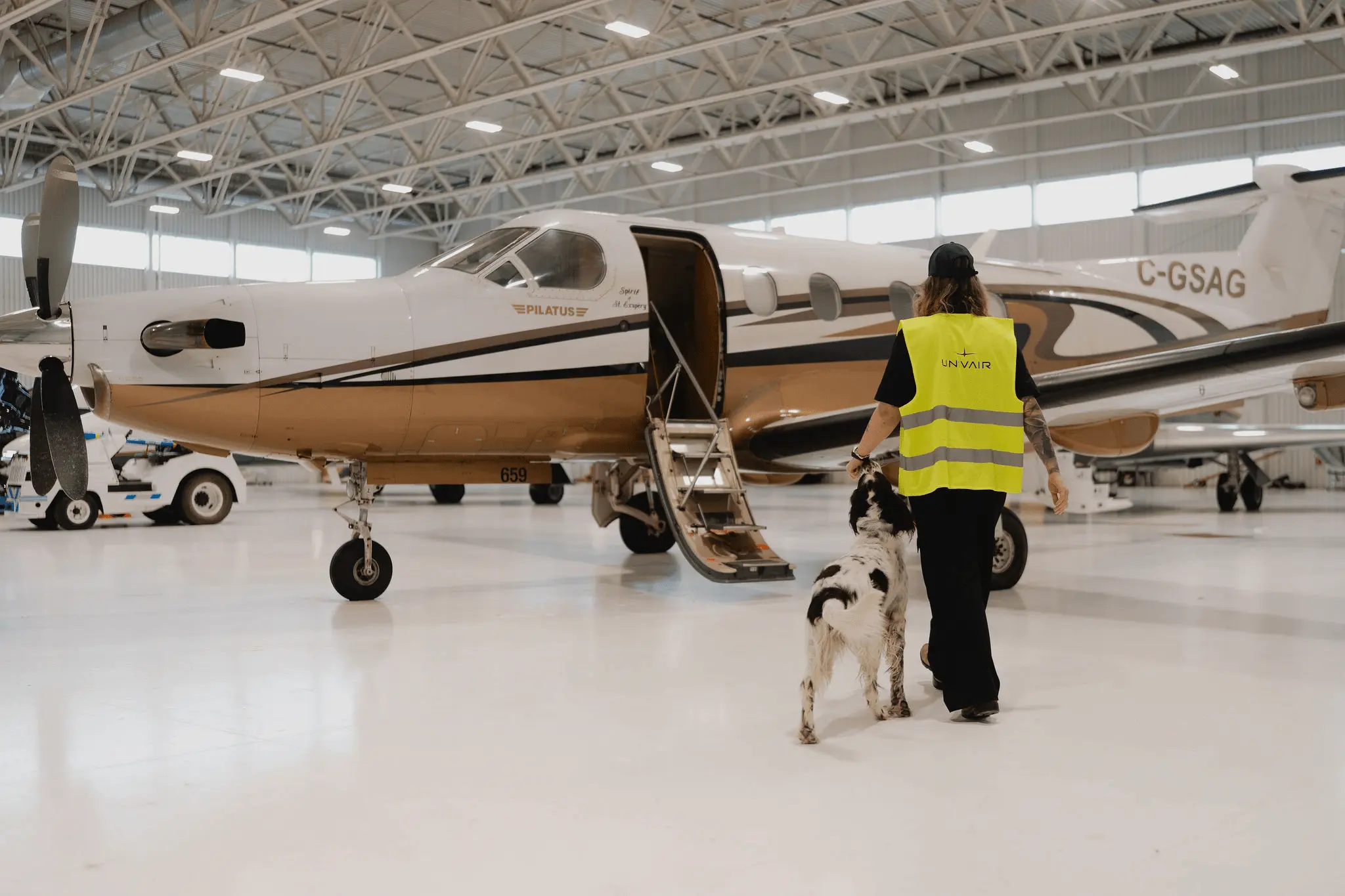Une employée avec un chien devant un avion dans un hangar